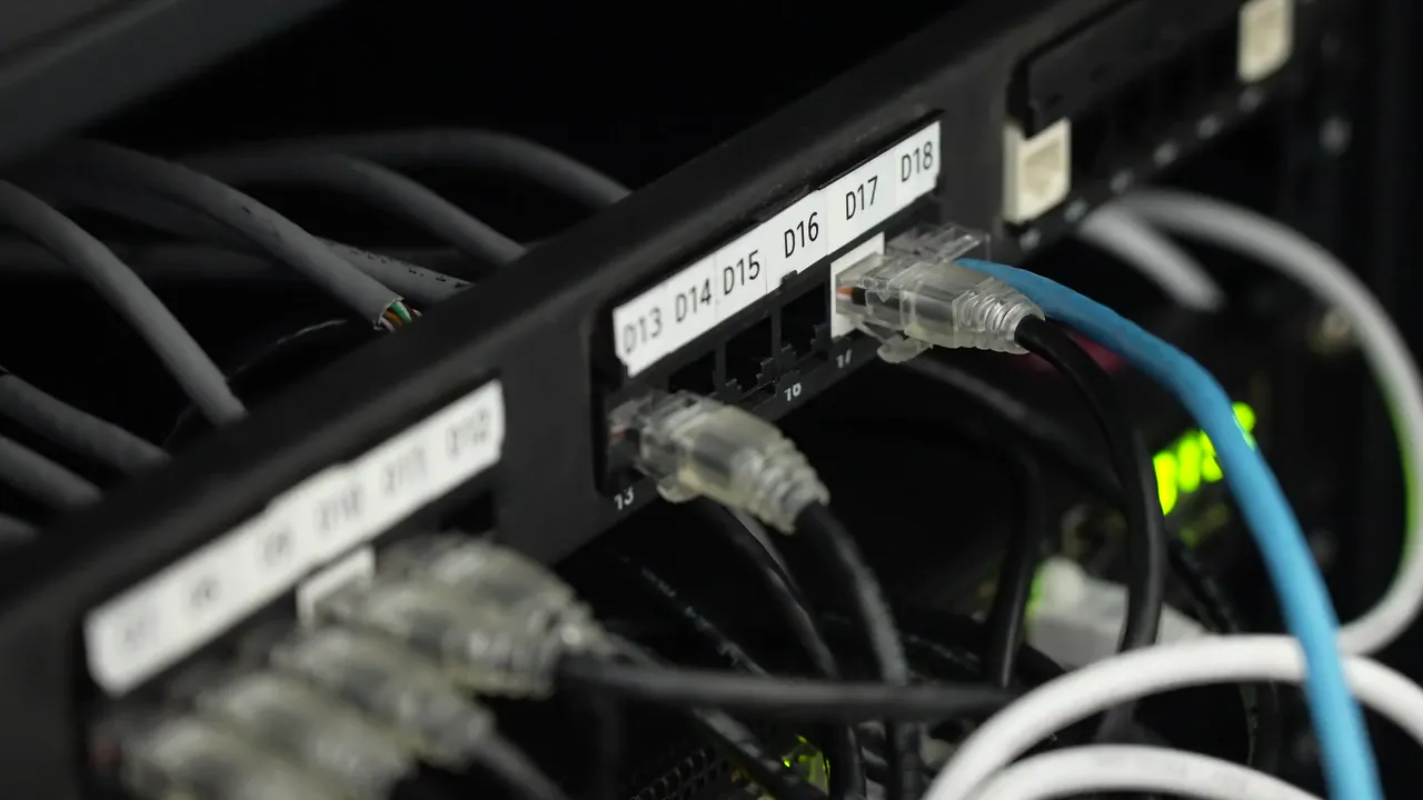 A hand plugs a patch cord into labelled ports D13 to D18